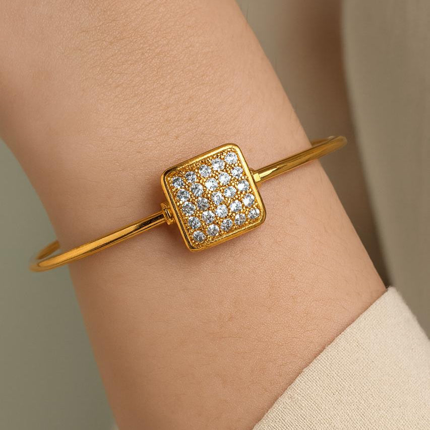 Gold bracelet with diamond accents on a wrist against a neutral background